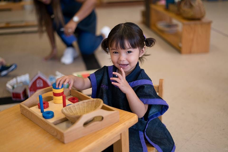 Child playing with colorful blocks on a wooden tray at a table
