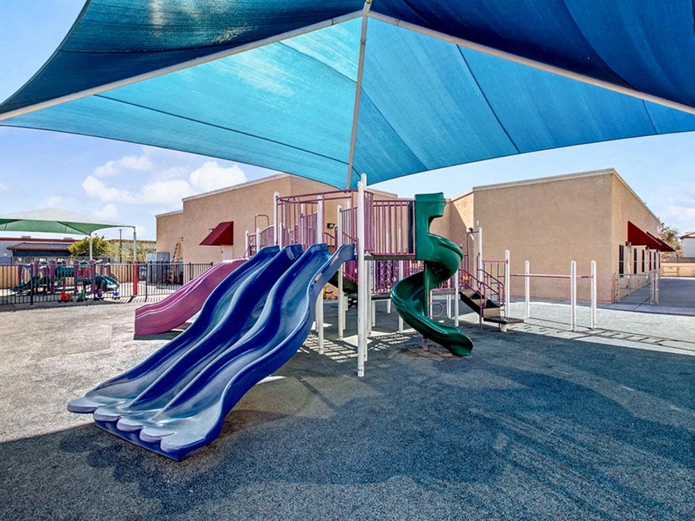 Playground with multiple slides, climbing structures, and a blue shade canopy overhead shade canopy