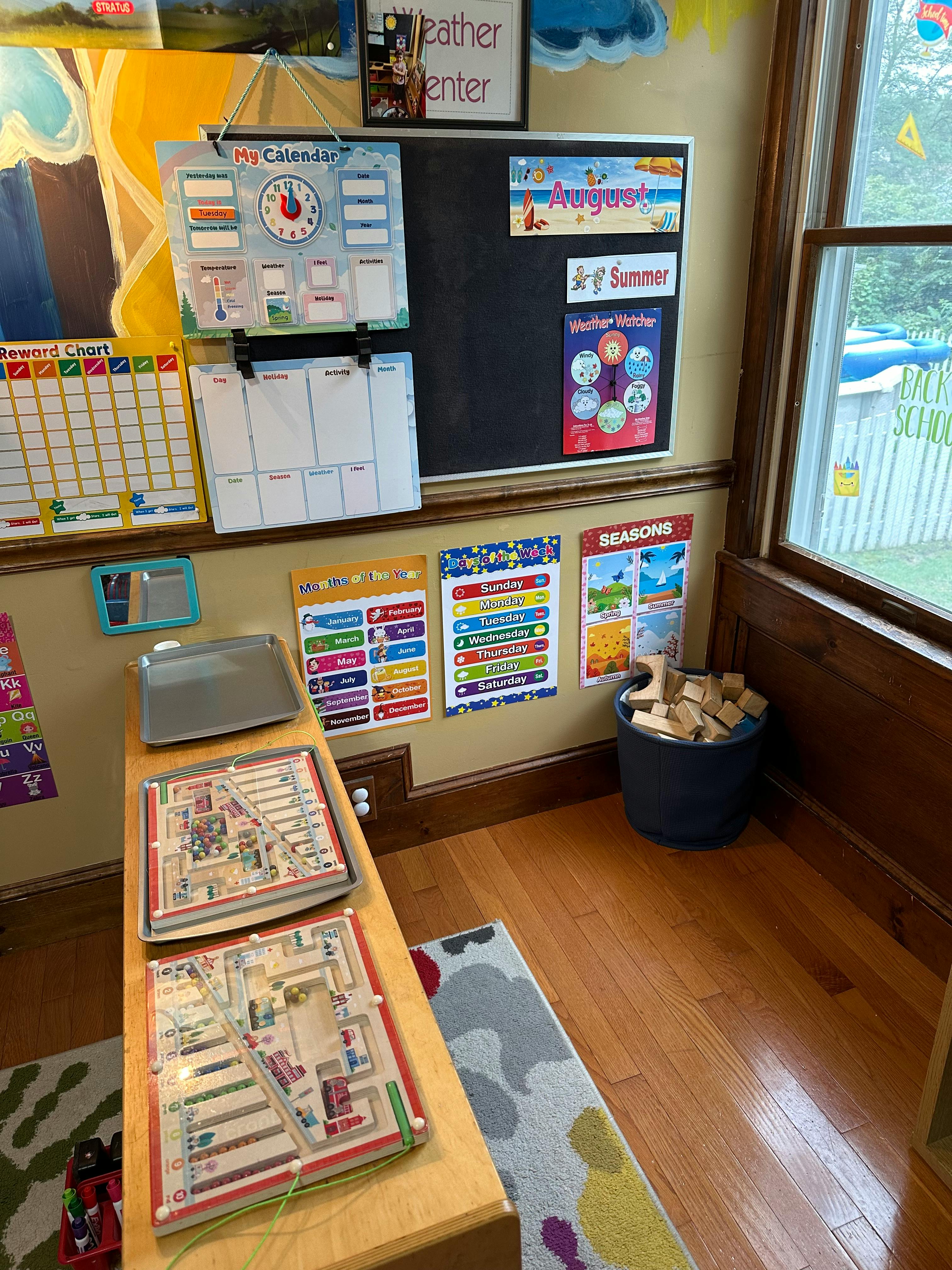 Classroom wall with calendar, charts, and a bucket of wooden blocks