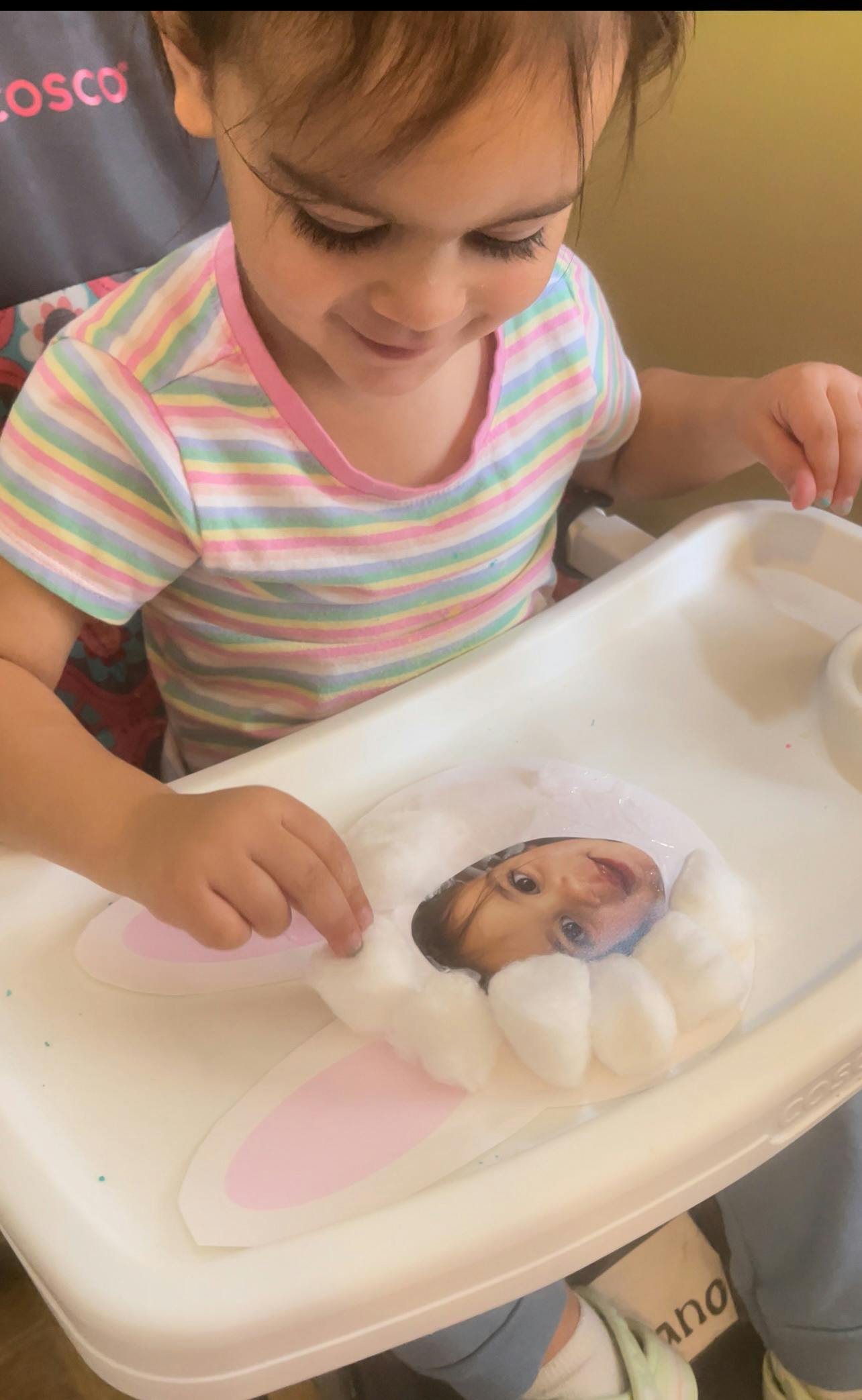 Child crafting with a cutout photo of a child and cotton balls