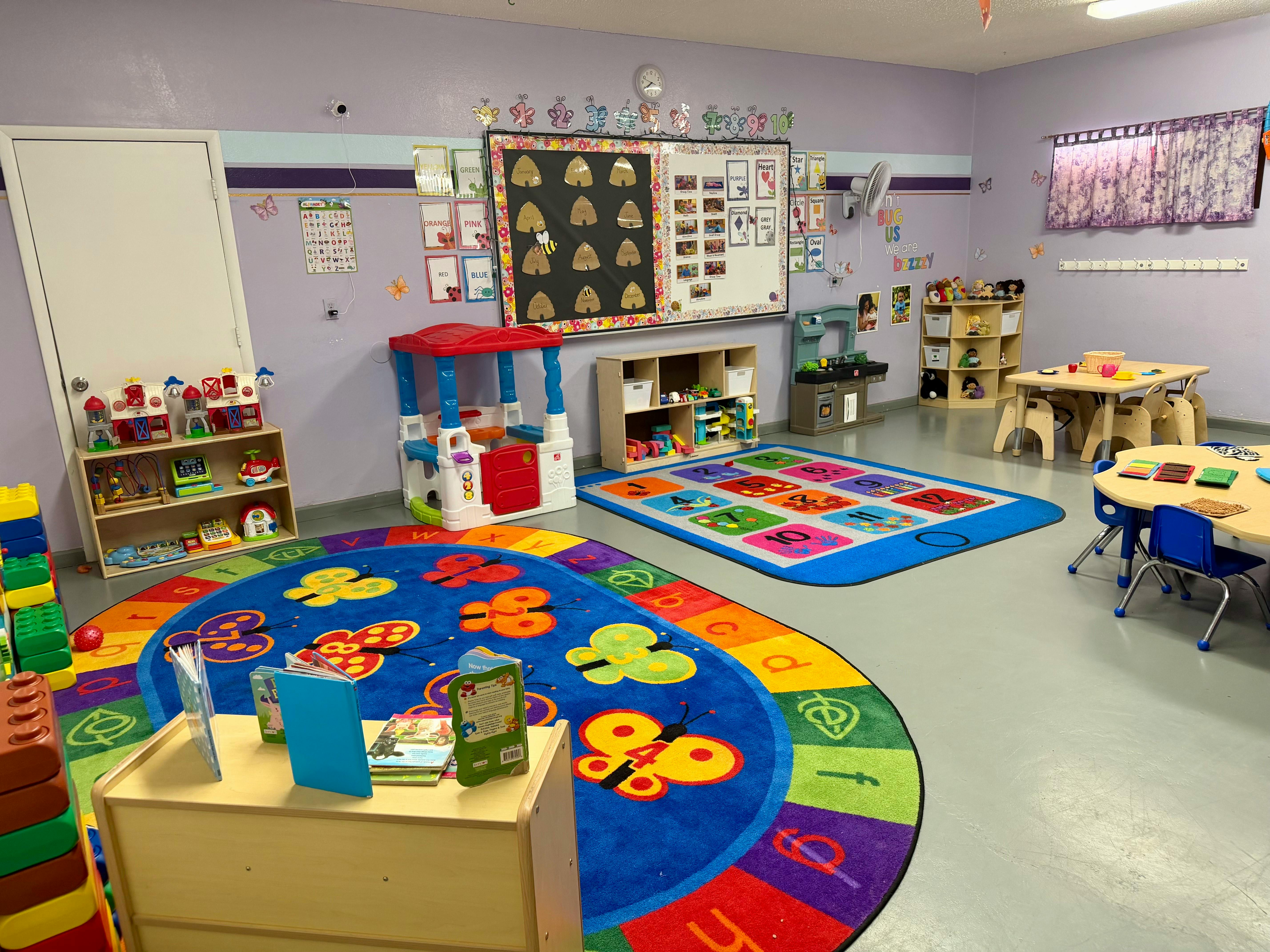 A classroom with several play areas, rugs with letters and numbers, and small tables with chairs