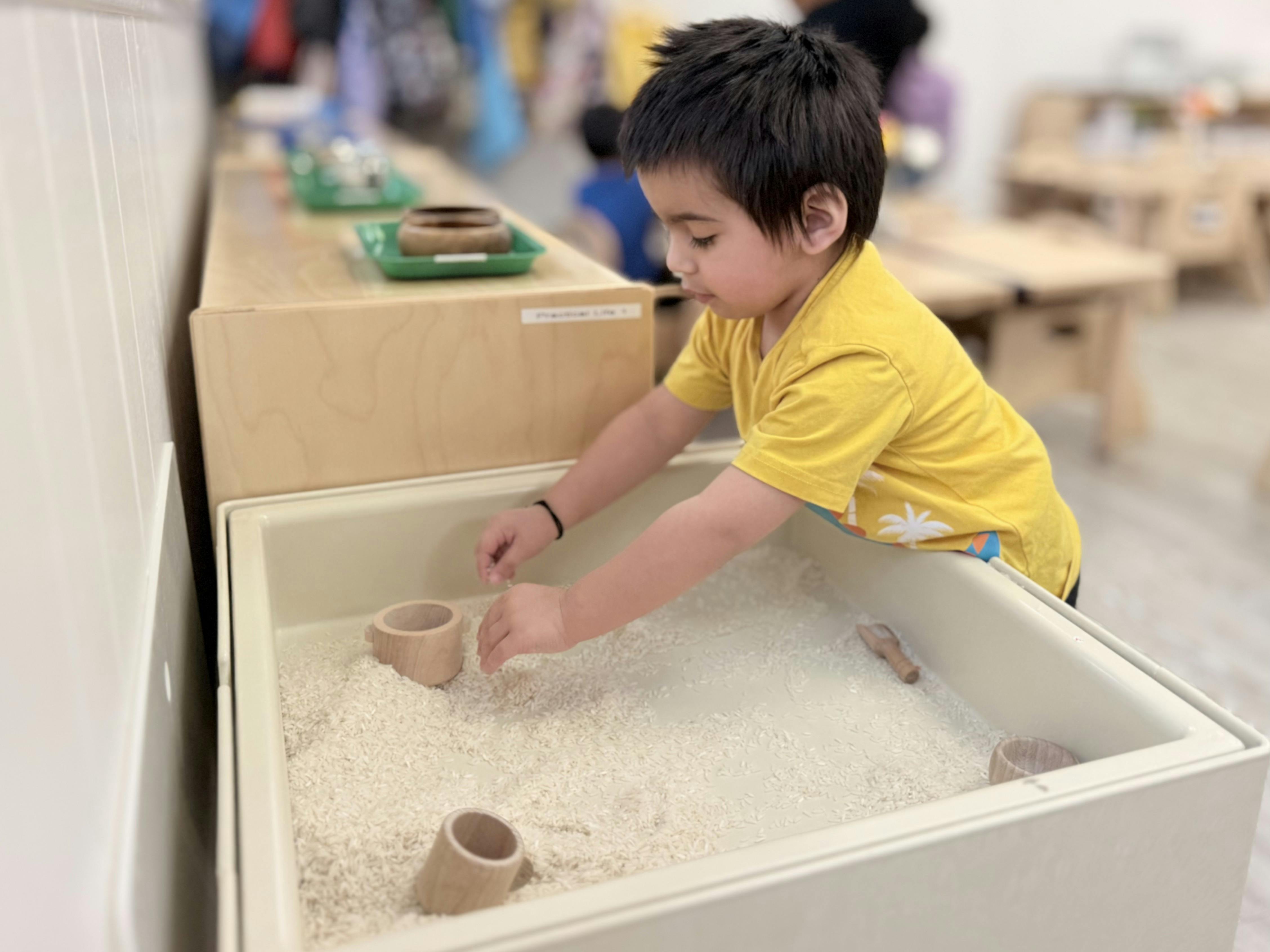 Child playing with rice and wooden cups in a sensory bin