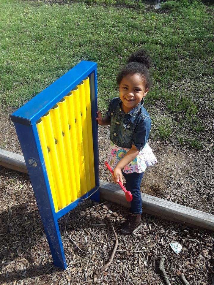 Child playing with a blue and yellow outdoor musical instrument
