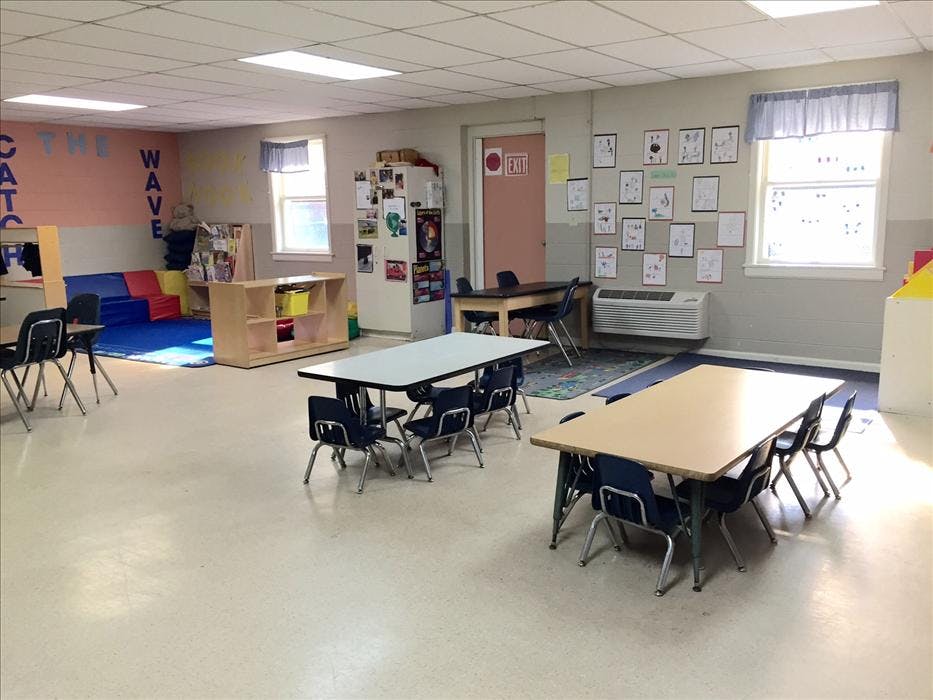 Classroom with child-sized tables and chairs, a reading corner, and student artwork