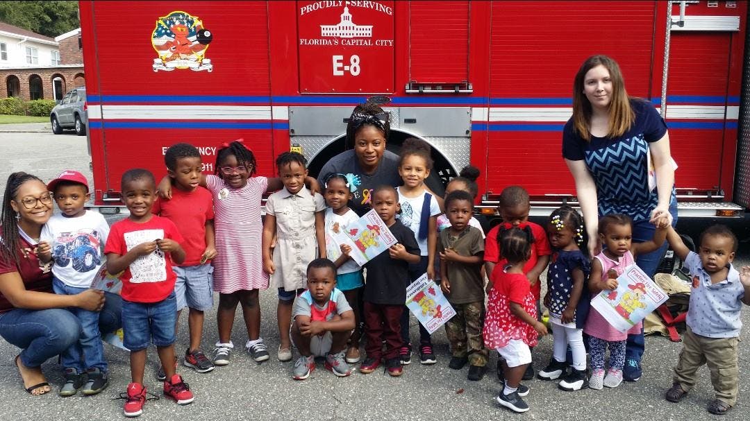 Two adults and many children standing in front of a fire truck