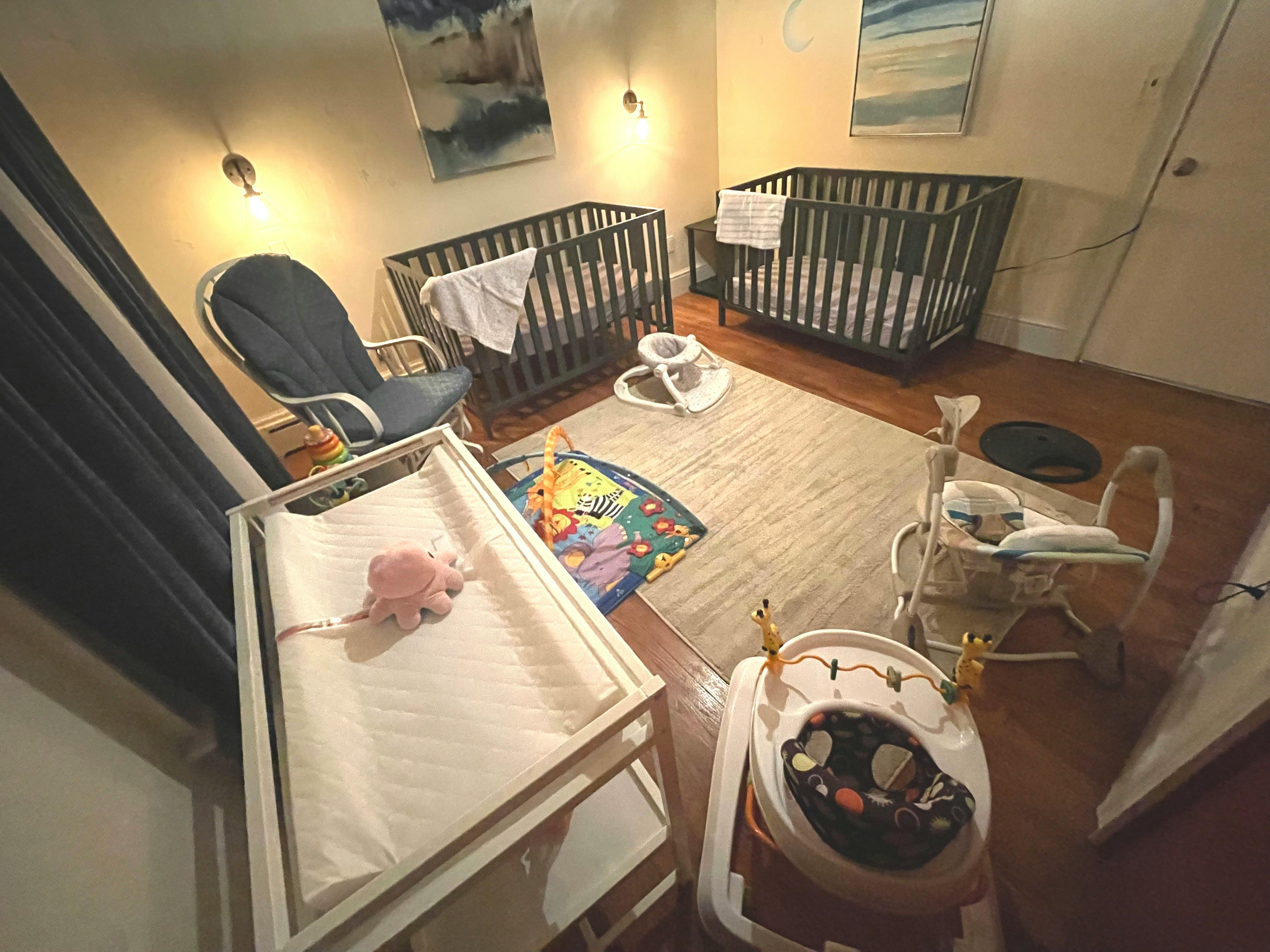 Nursery room with two cribs, a changing table, and baby play equipment
