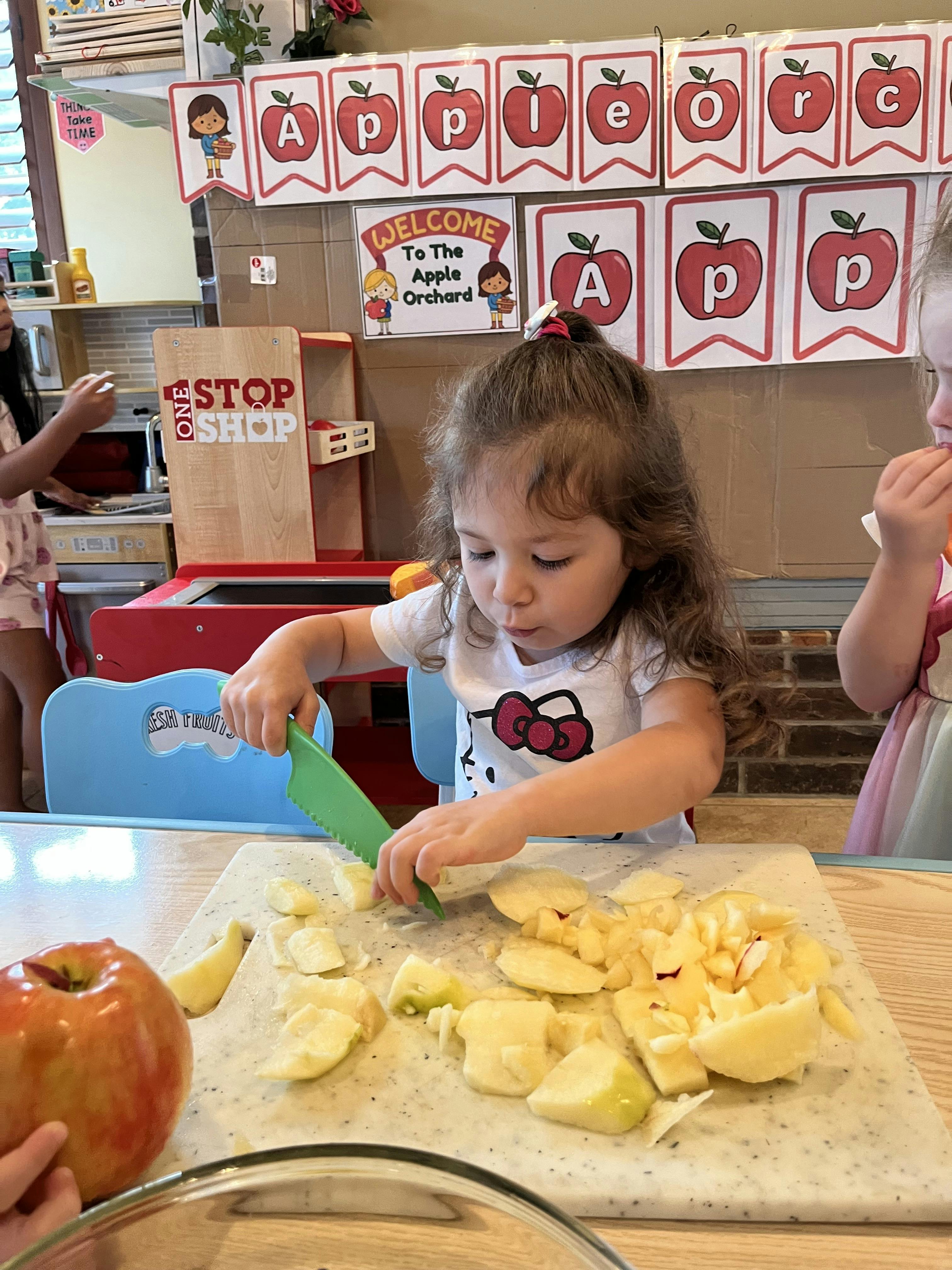 Child cutting apple pieces on a cutting board with a green knife