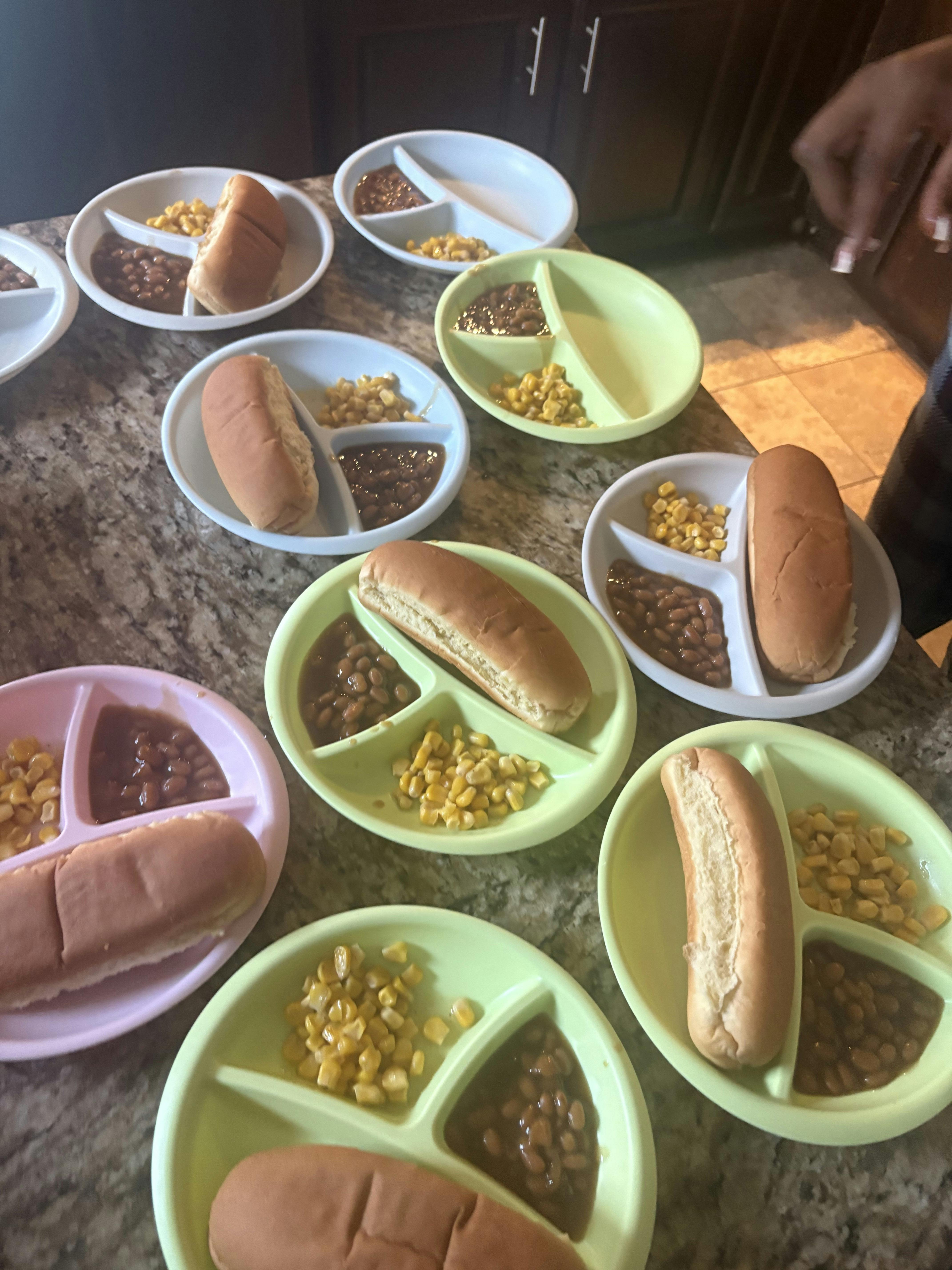 Multiple divided plates containing hot dog buns, corn, and beans
