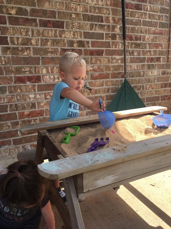 Child playing in a sandbox with a blue shovel