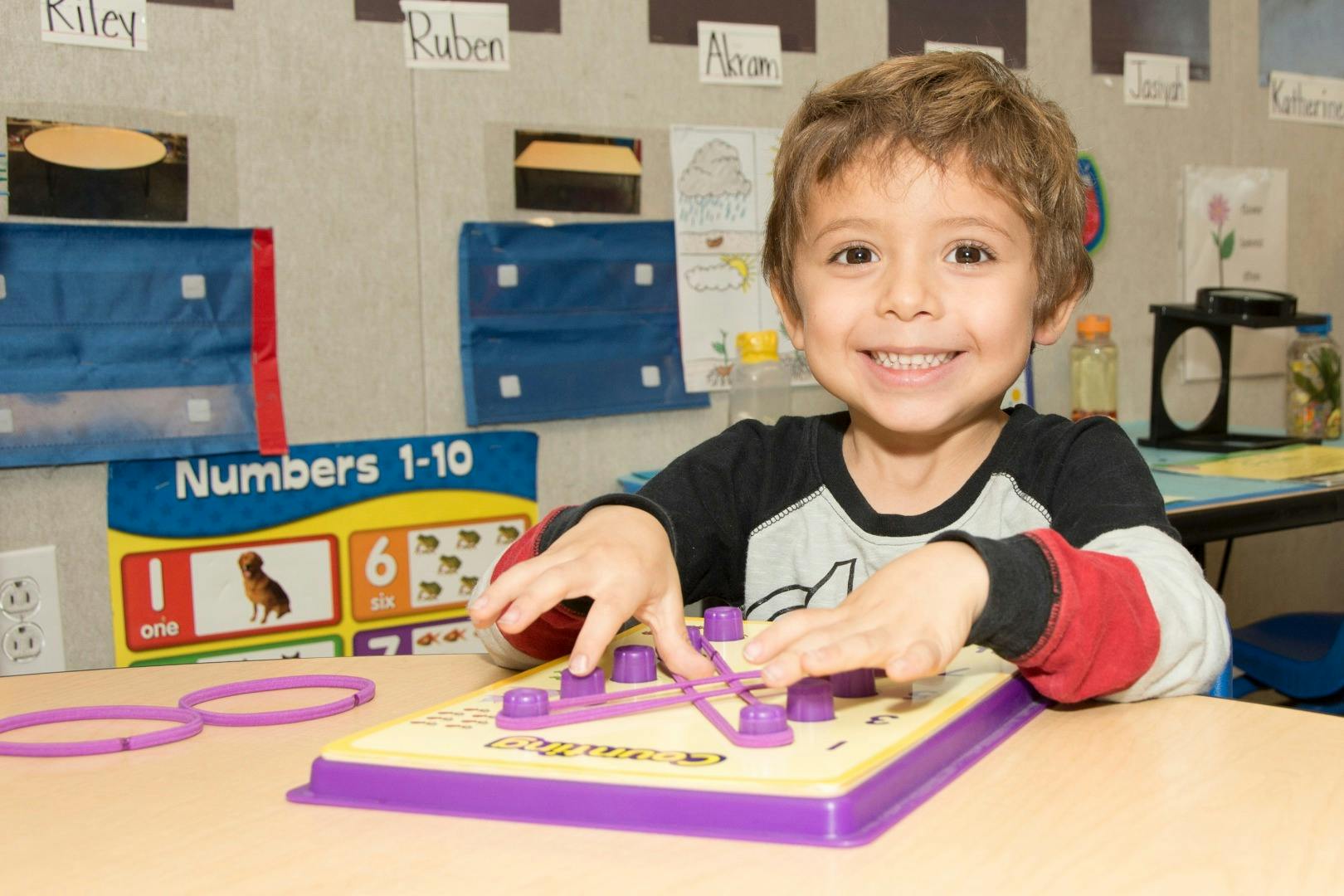Child playing with a geoboard at a table