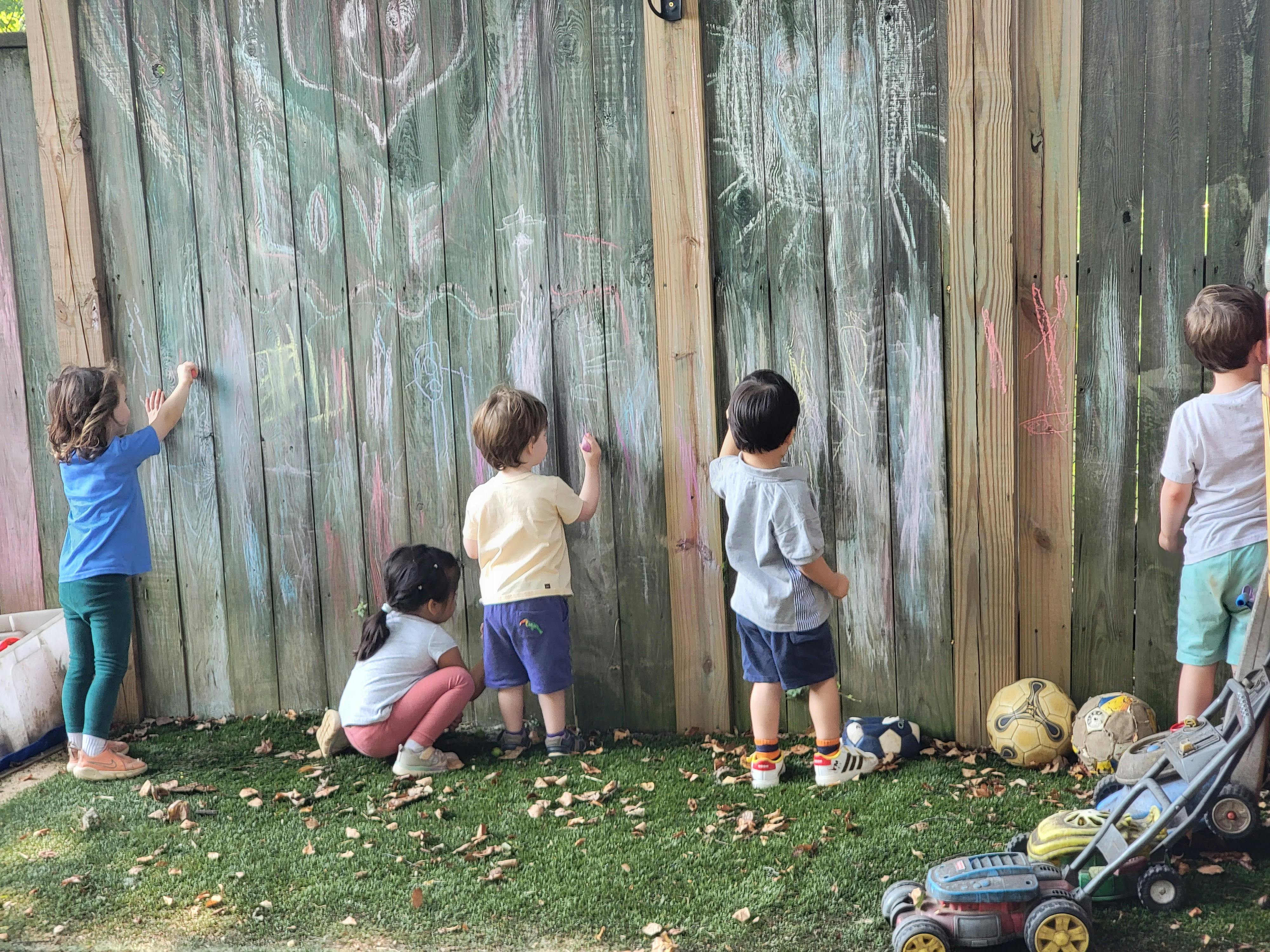 Children drawing on a wooden fence with chalk