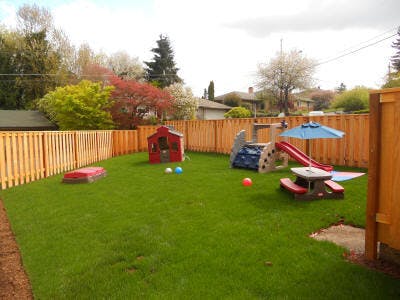 Backyard with a wooden fence, playhouse, slide, and picnic table