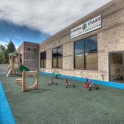 Playground with small riding toys and a building with a "Strong Start" sign