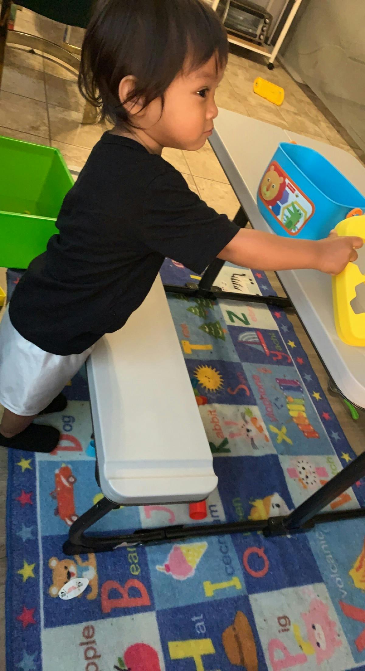 Child leaning against a small bench while playing with toys on a table