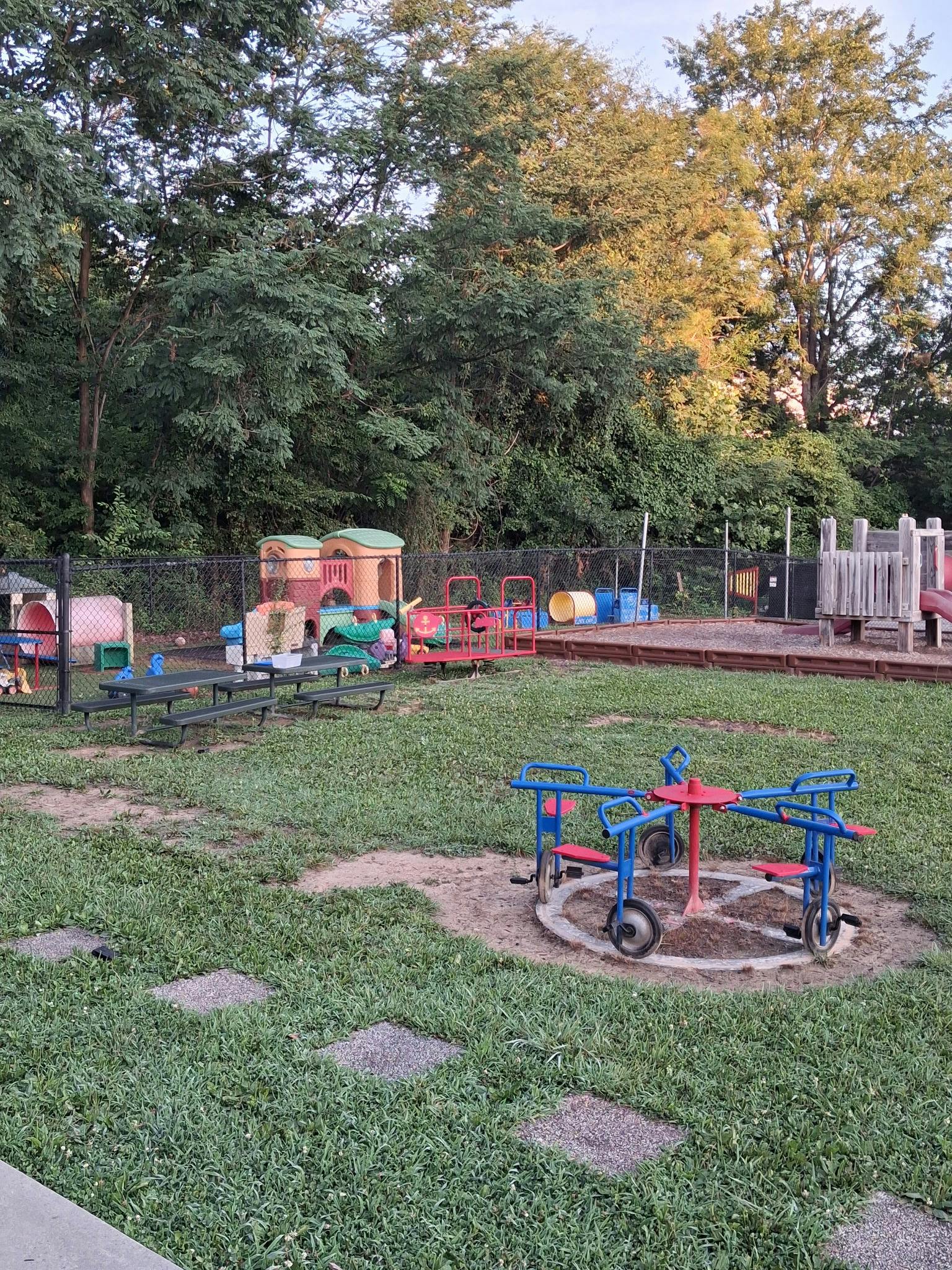 Empty outdoor playground with a merry-go-round, play structures, and picnic table