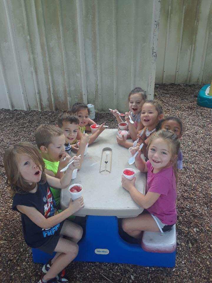 Children sitting at a table eating from cups with spoons