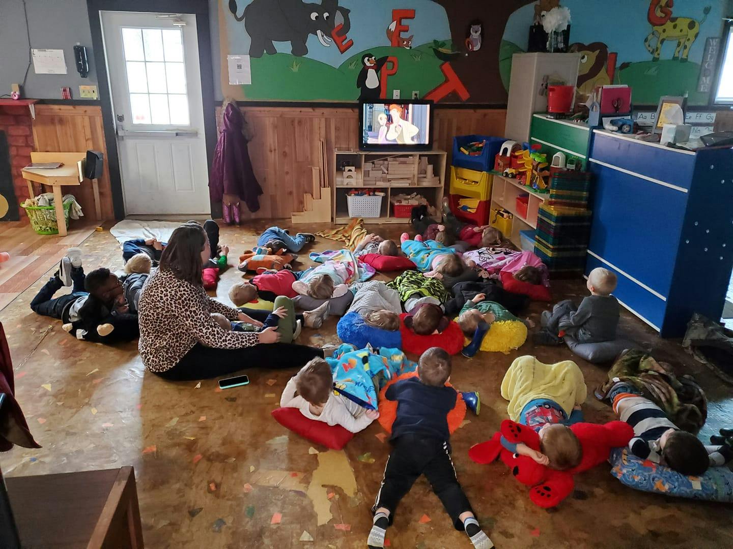Person sitting on floor with multiple children lying on floor around them