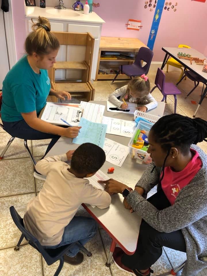 Three adults and two children working at tables in a classroom