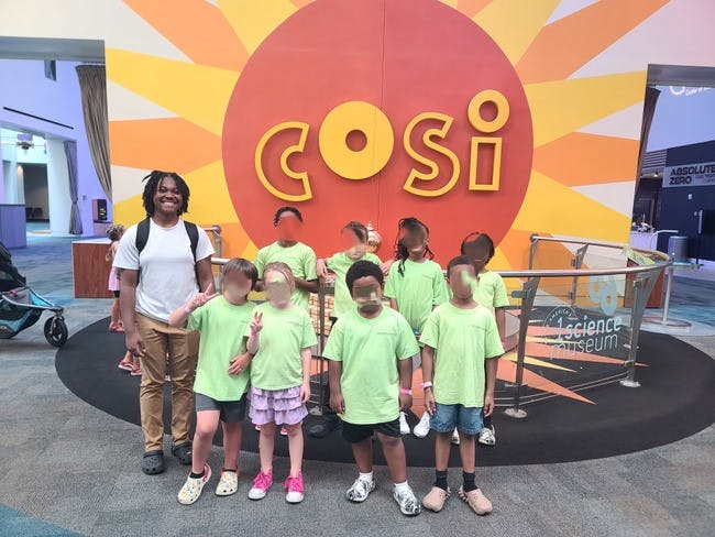Person and children in front of a COSI sign