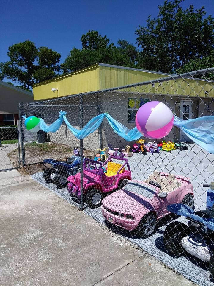 Chain link fence with blue fabric and beach balls, toy cars behind it