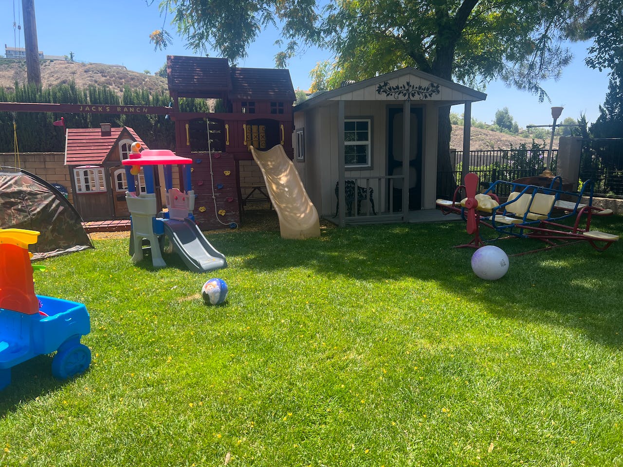 Backyard with a playset, playhouse, and swing set on green grass