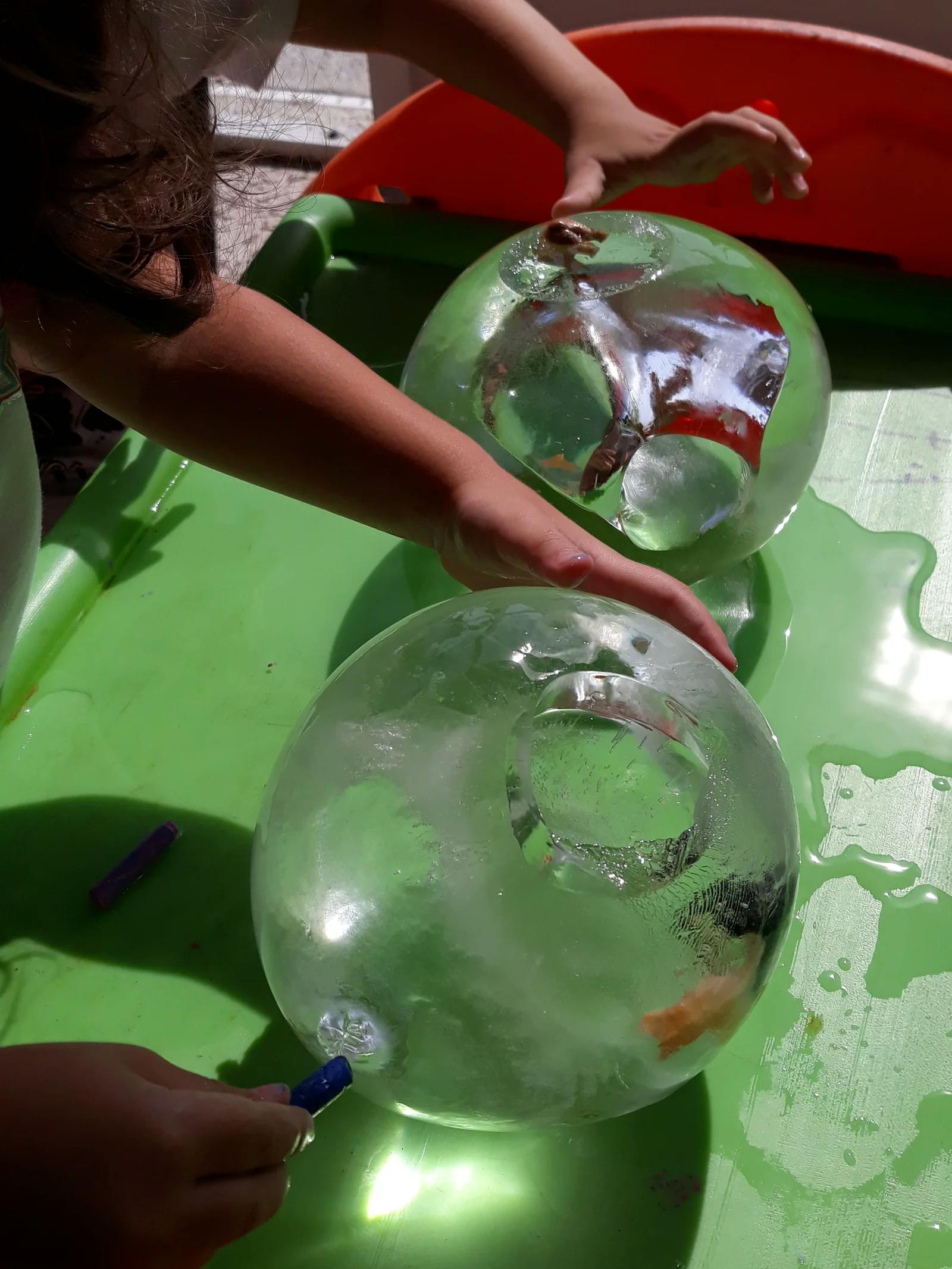 Person holding two clear ice spheres with objects frozen inside