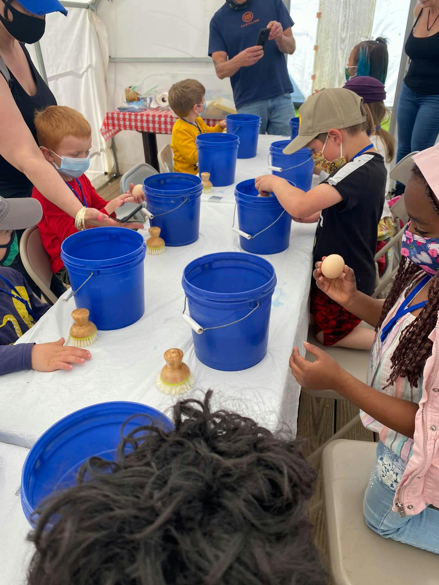 Children and adults at a table with blue buckets and brushes