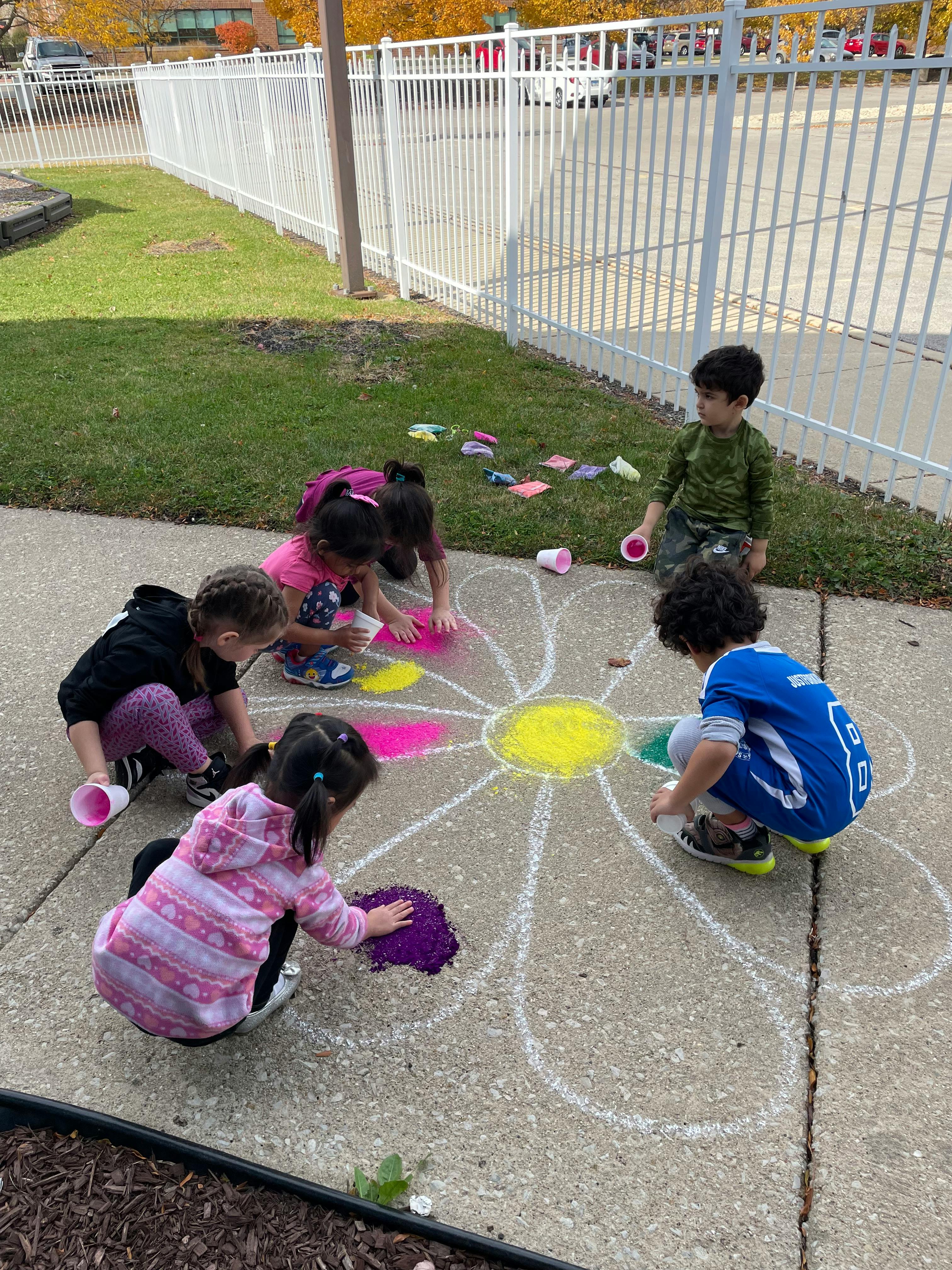 Children coloring a chalk flower on a sidewalk