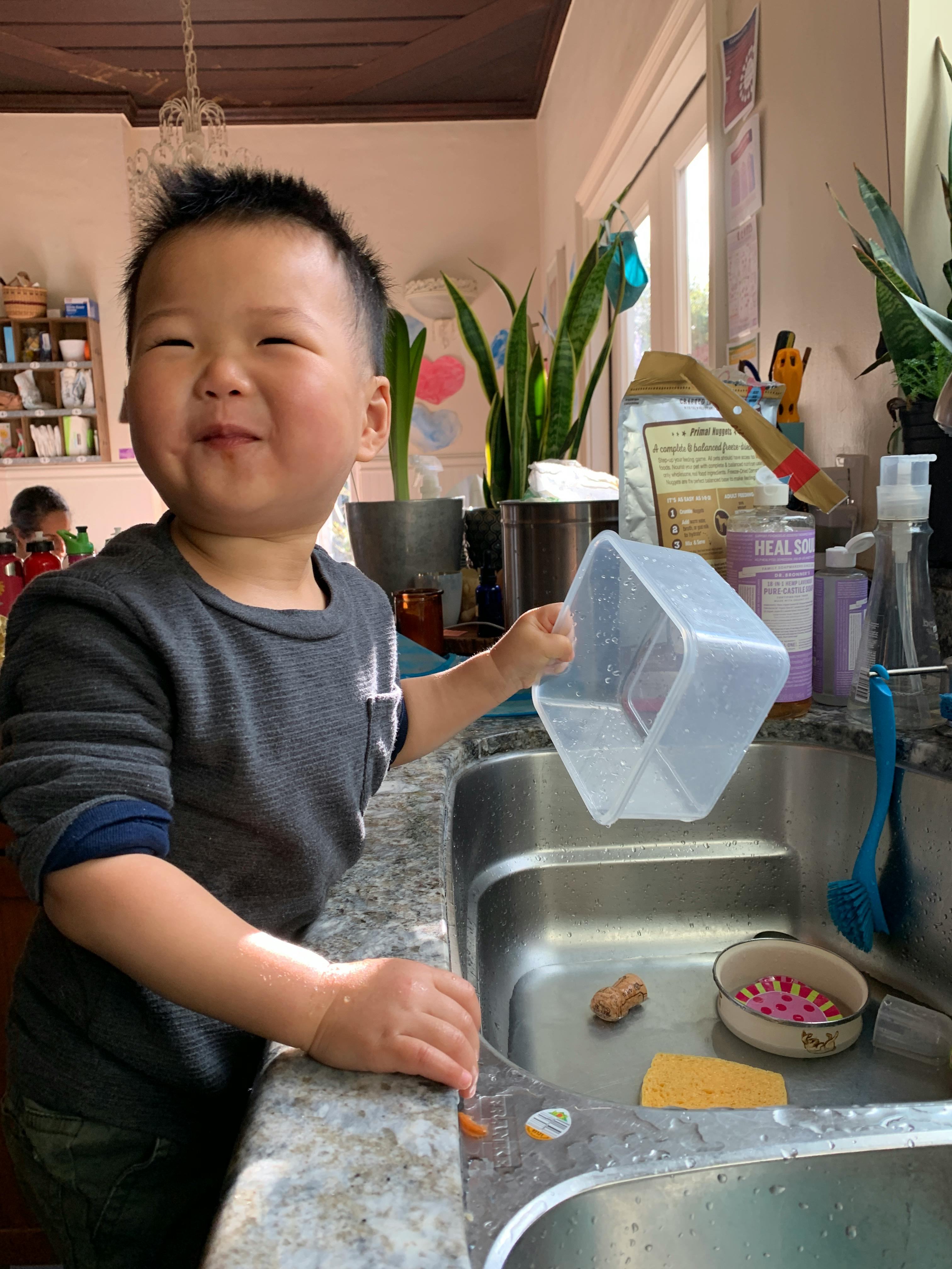 Child holding a plastic container over a kitchen sink