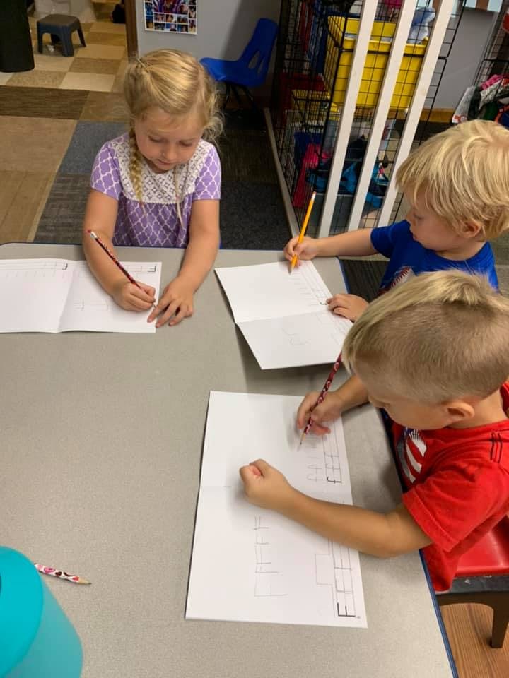 Three children writing on paper with pencils at a table