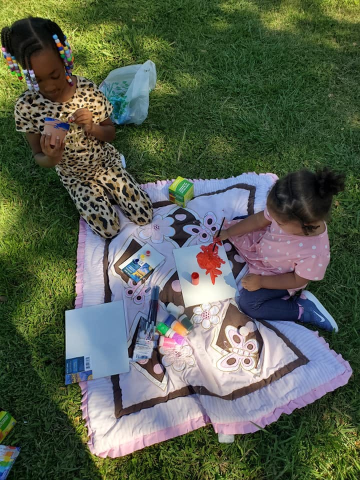 Two children painting and drawing on a blanket outdoors