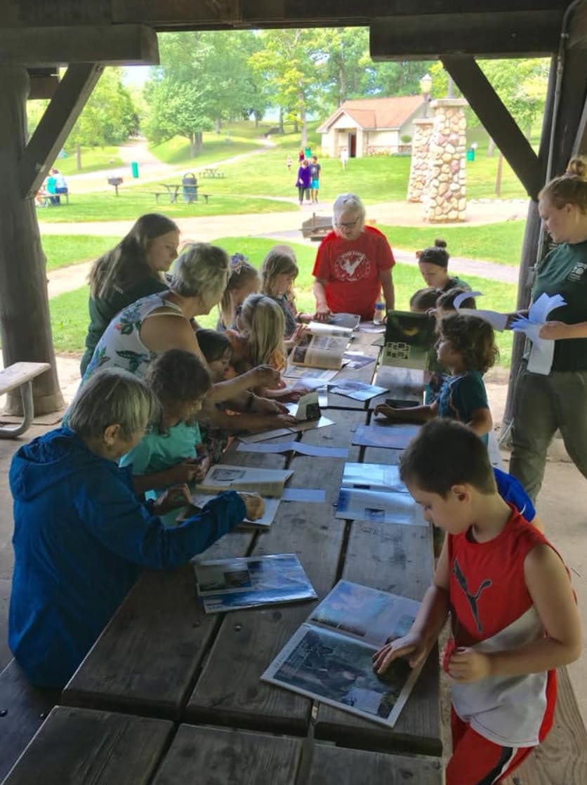People and children gathered around a long wooden table with papers