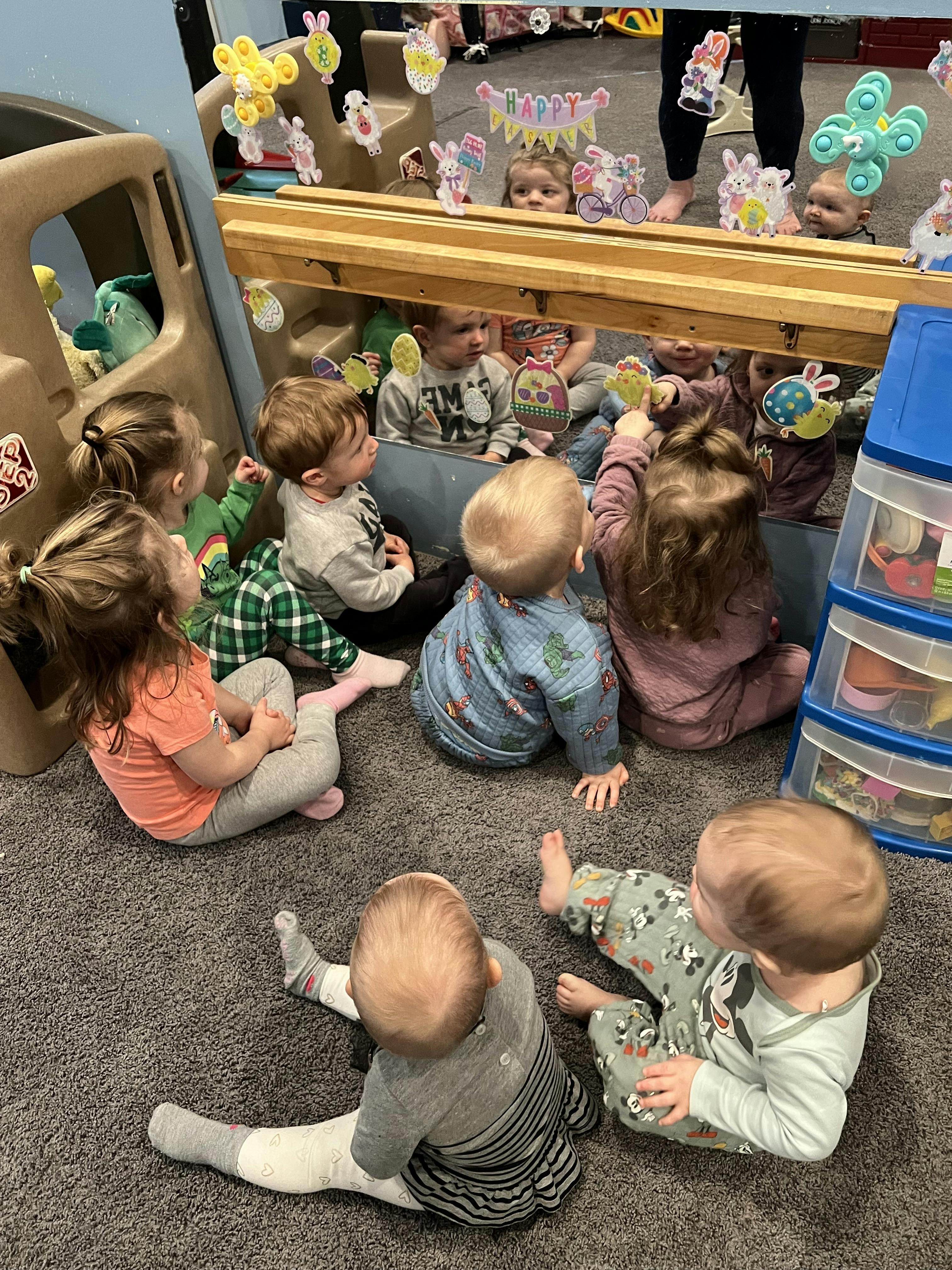 Multiple children sitting on the floor looking at their reflections in a low mirror