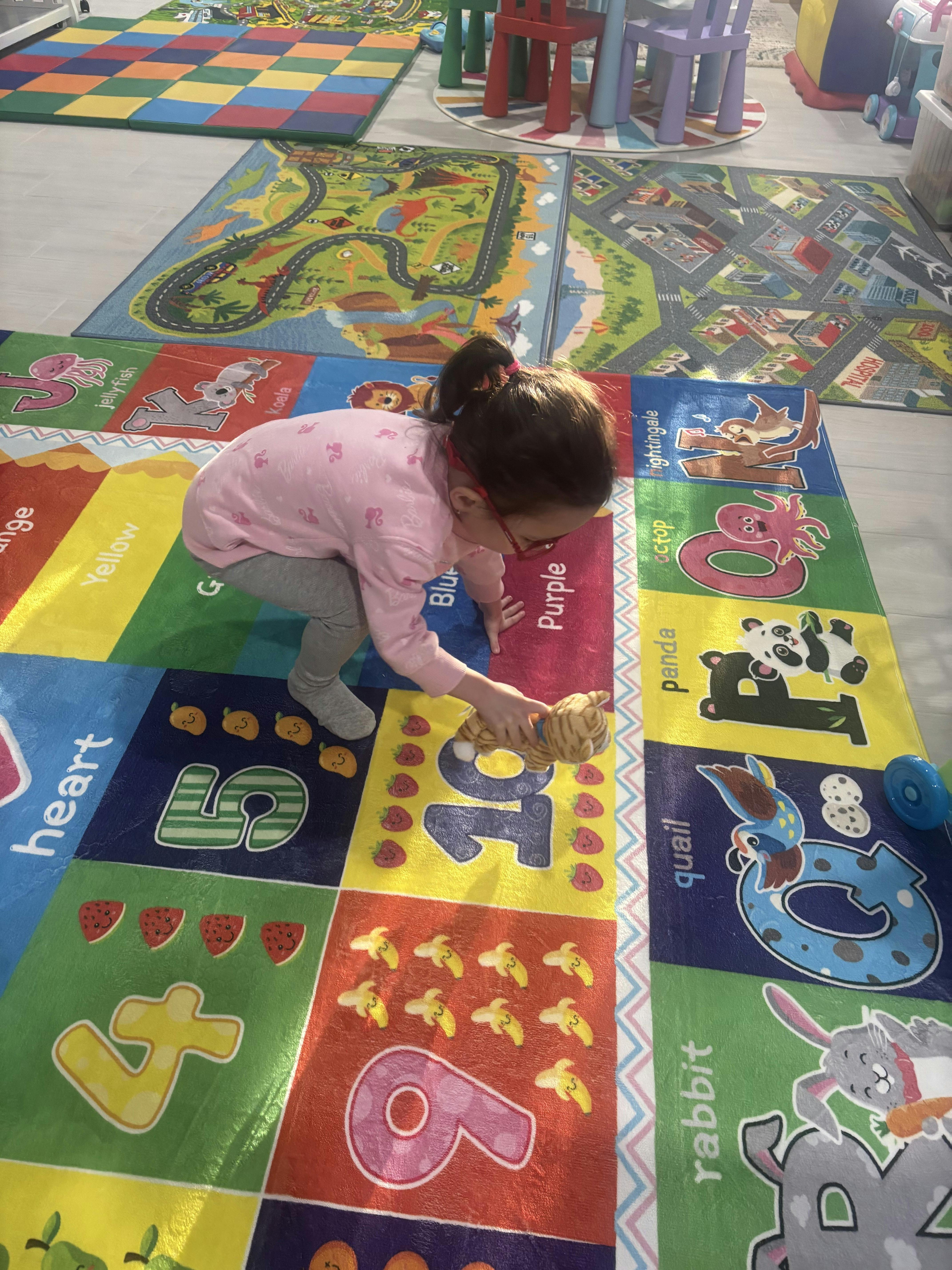 Child playing with a stuffed animal on a colorful number and letter mat