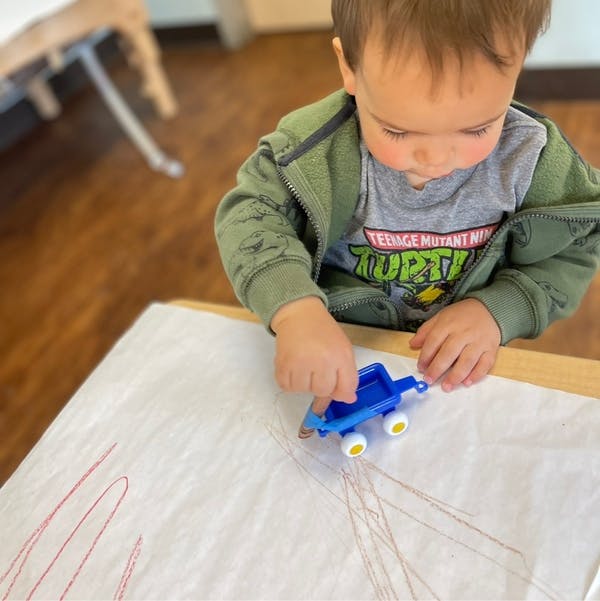 Child playing with a toy truck on paper