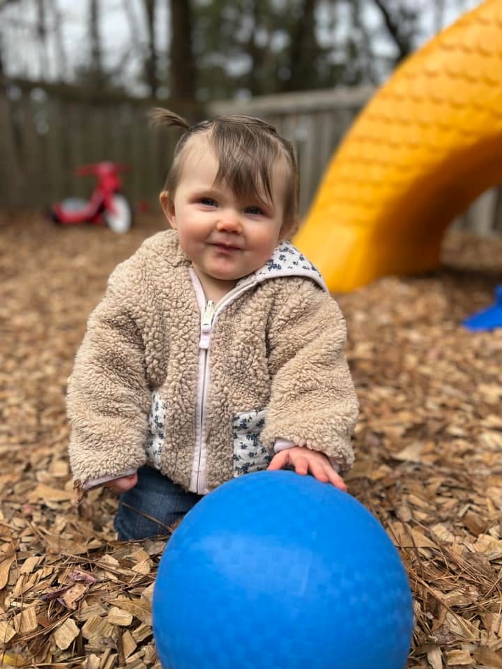 Child kneeling on wood chips with a blue ball