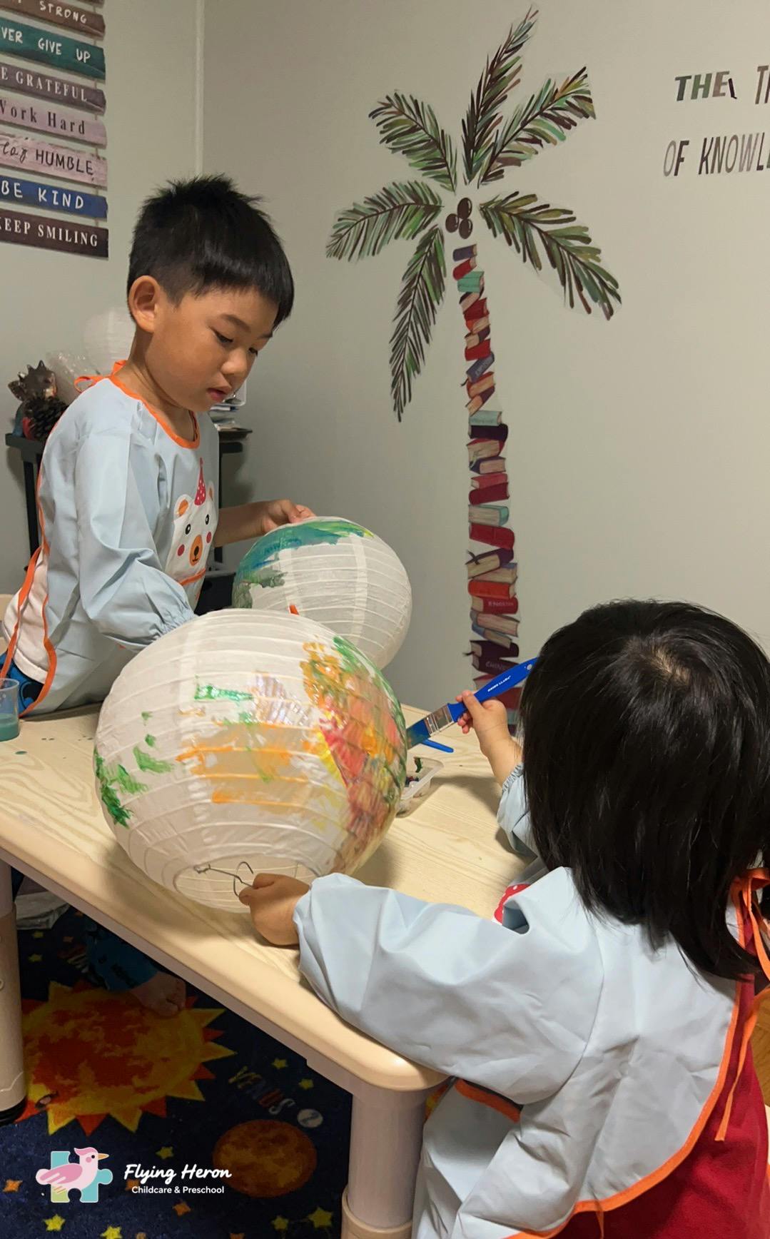 Two children painting paper lanterns at a table