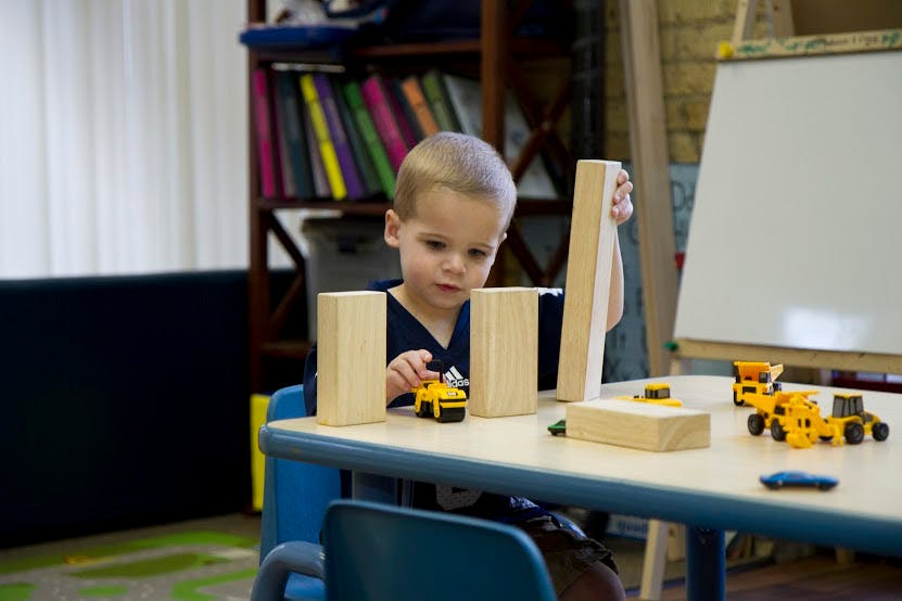 Child playing with wooden blocks and toy trucks at a table