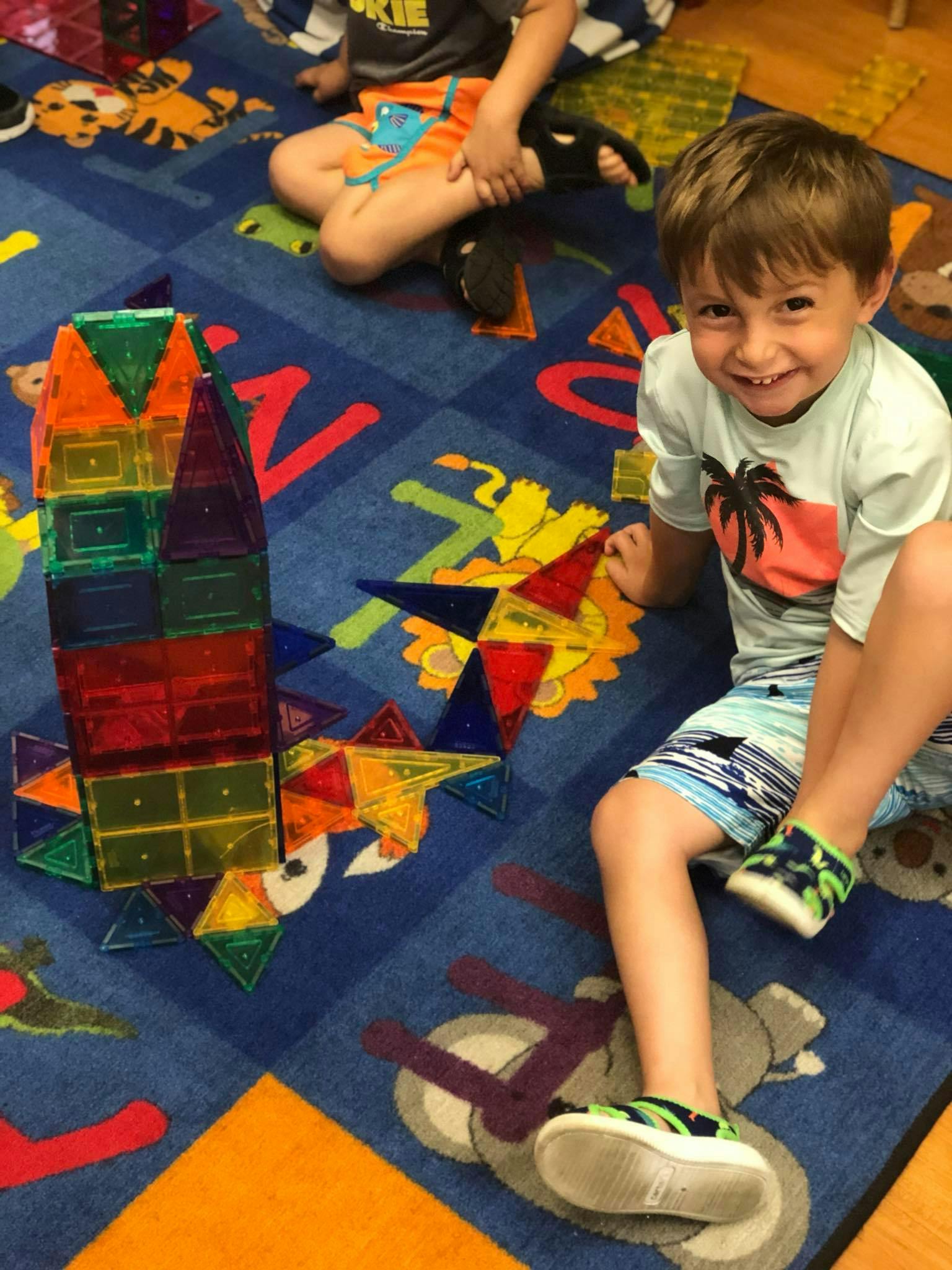 Child sitting on a colorful rug next to a tall structure made of magnetic tiles
