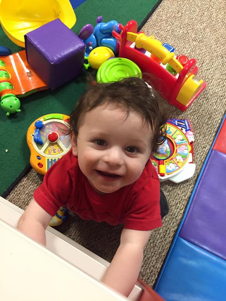 Child in red shirt crawling on floor with toys