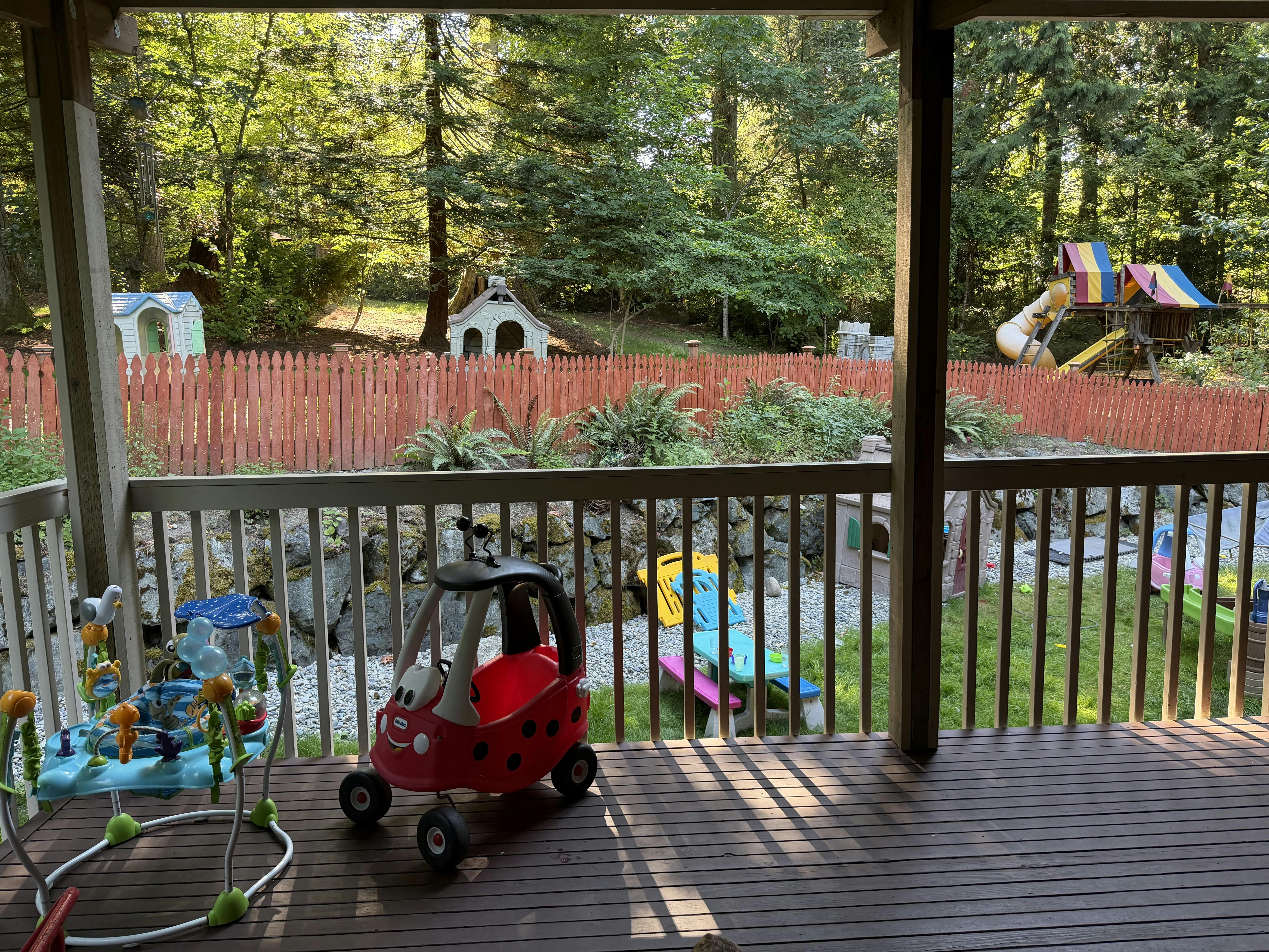 Play equipment on a deck and in a fenced backyard