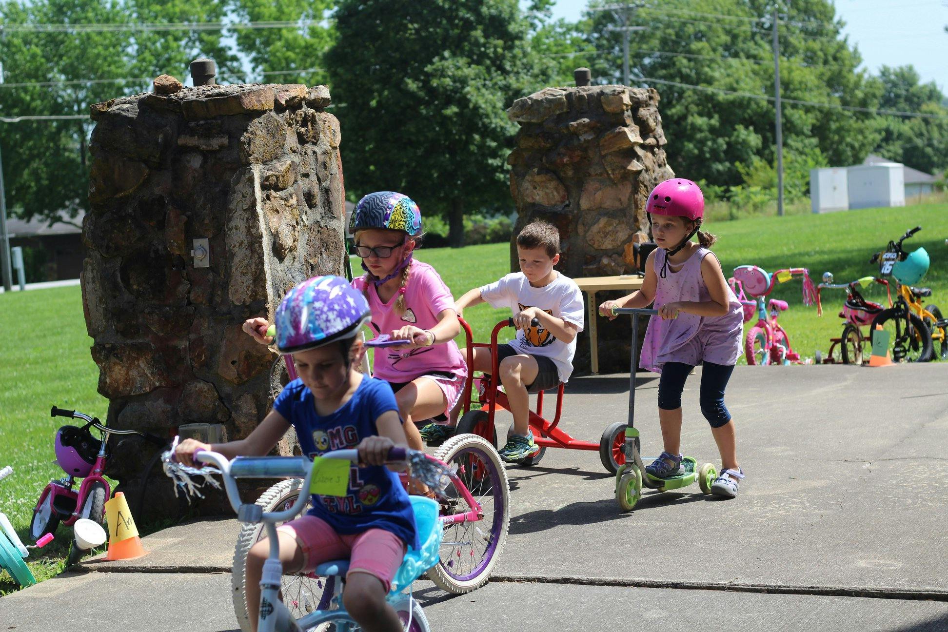 Children playing outdoors with bikes, tricycles, and scooters