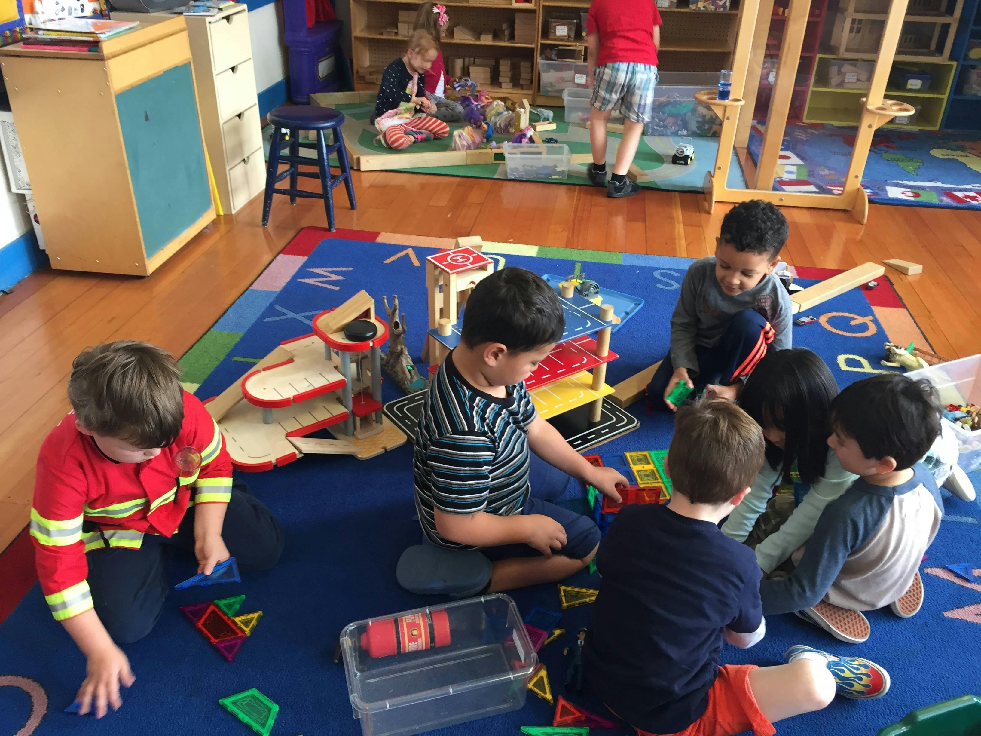 Children playing with toys on a blue rug in a classroom