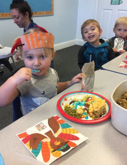 Child in a paper hat eating at a table with other children