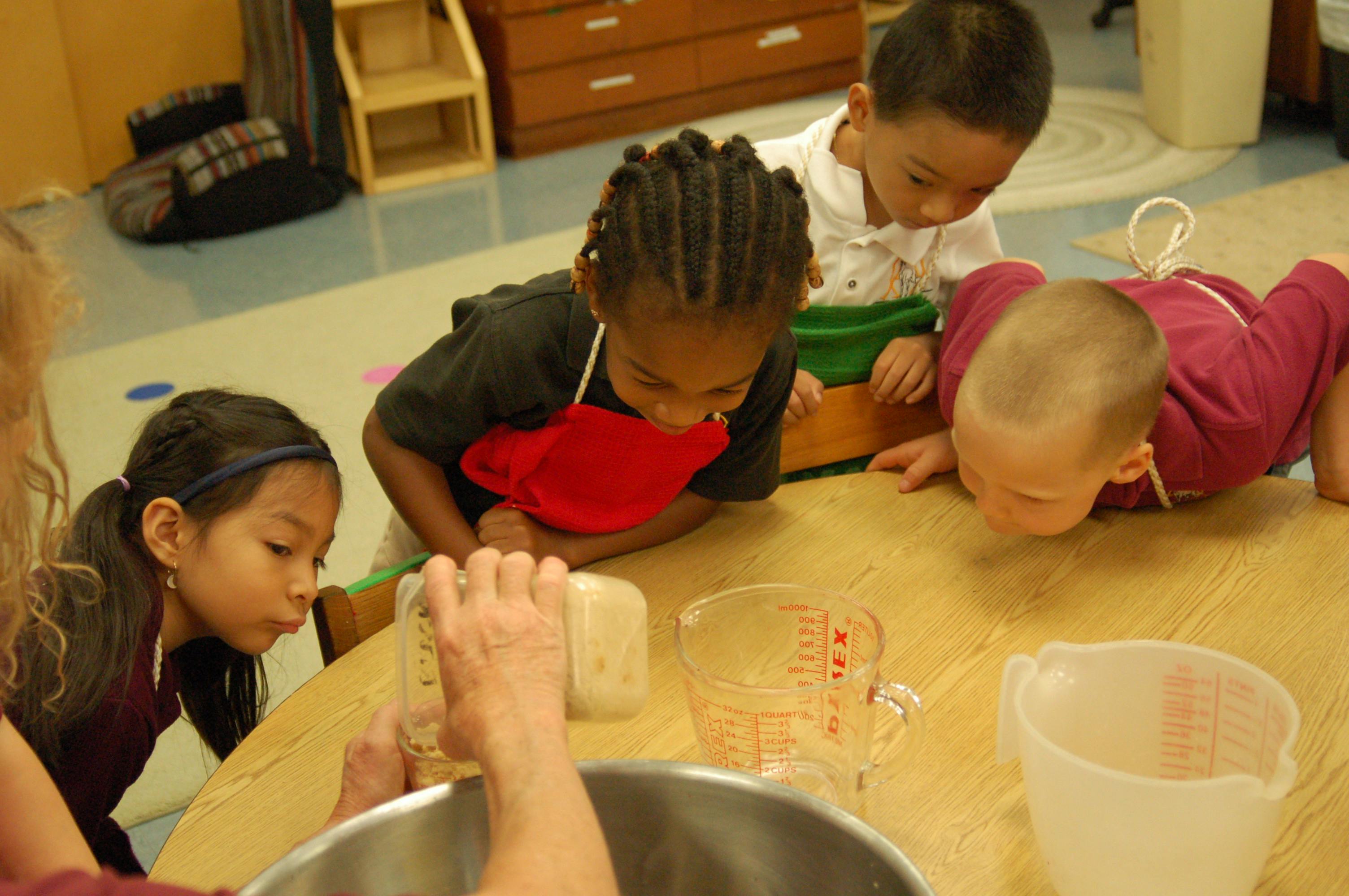 Children watching an adult pour ingredients into a bowl