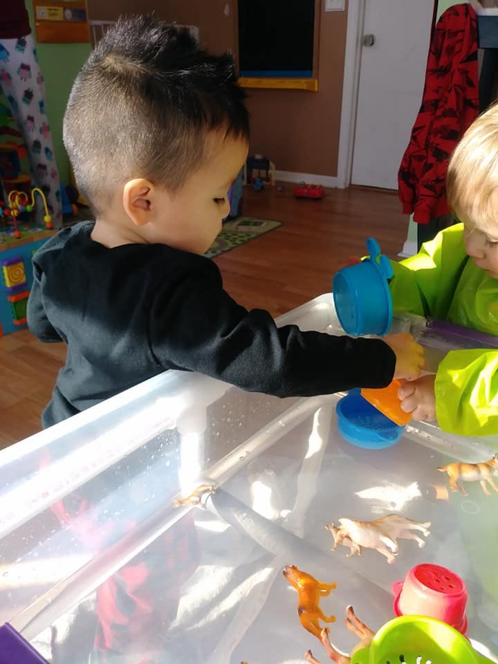 Two children playing with toys in a water table