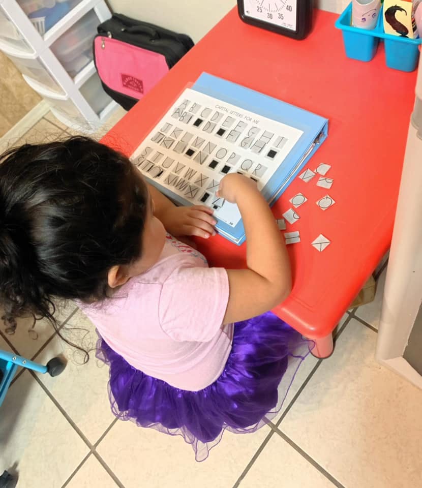Child playing with letter tiles on a red table