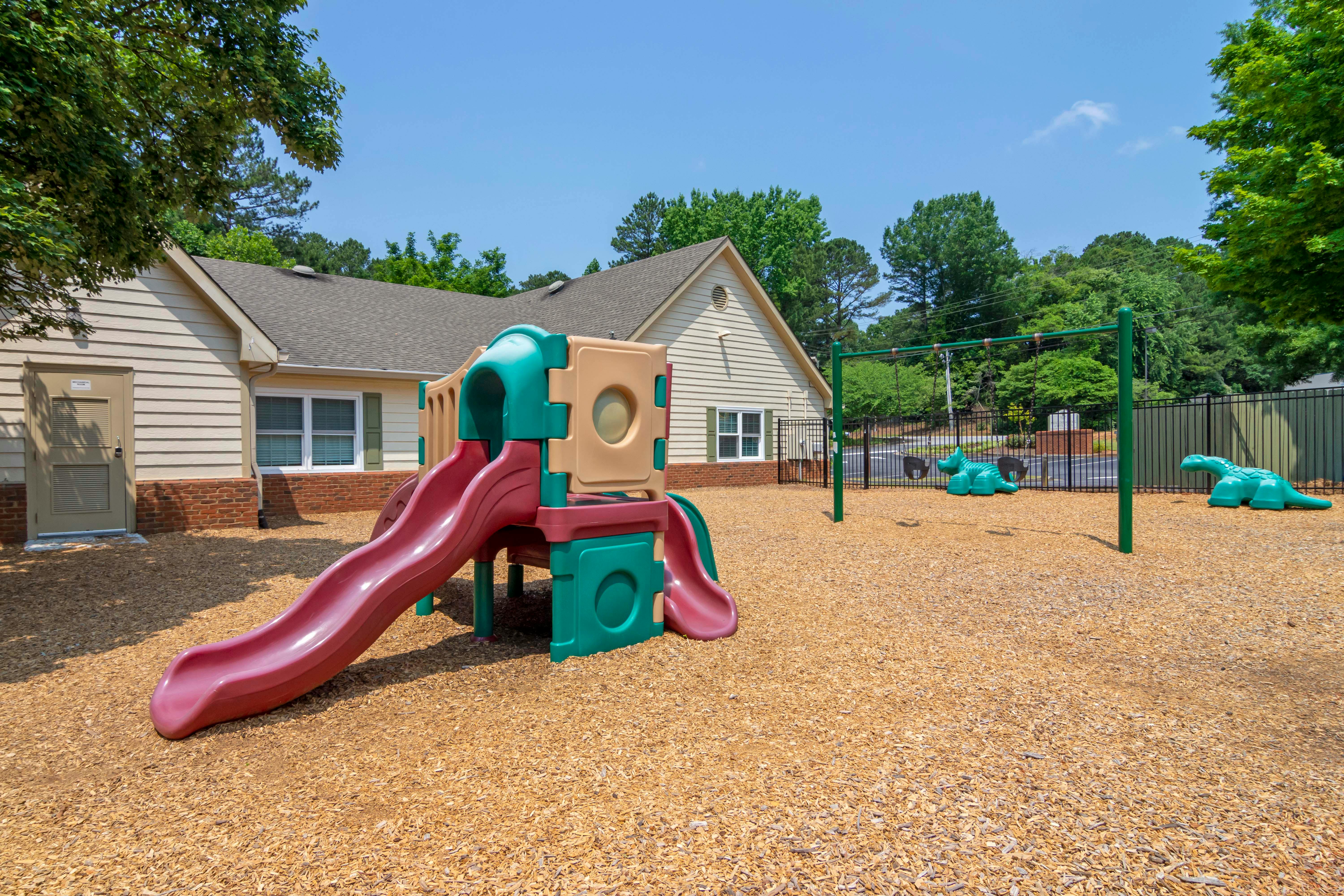 Playground with slides, swings, and dinosaur spring riders on wood chips
