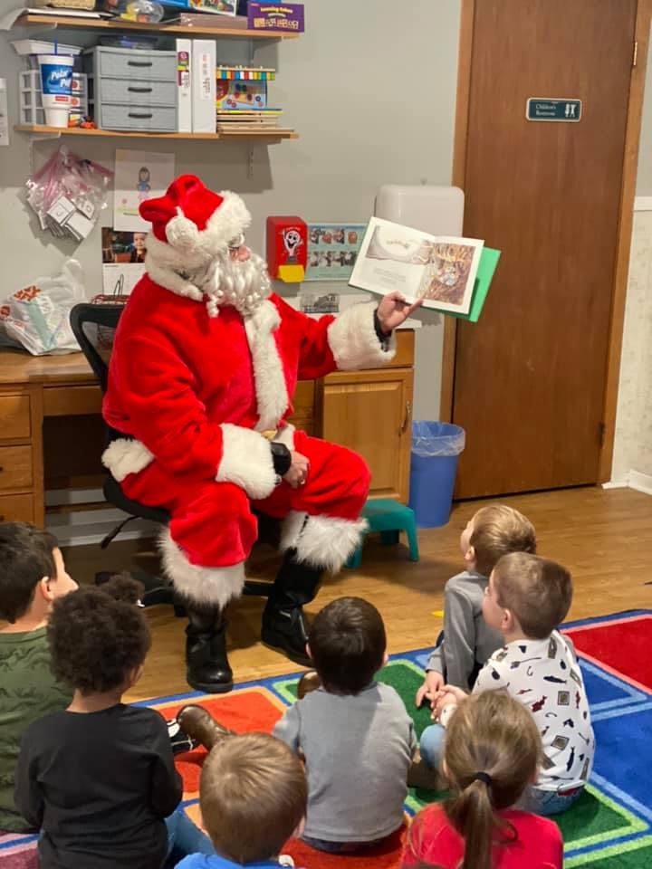 Person dressed as Santa Claus reading a book to a group of children