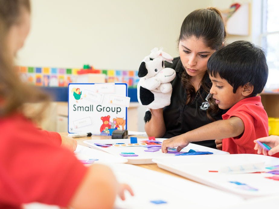 Adult with a puppet and a child playing with shapes at a table, "Small Group" sign